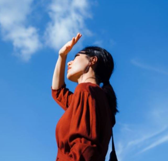 Woman looking at the sky covering her eyes with one hand.